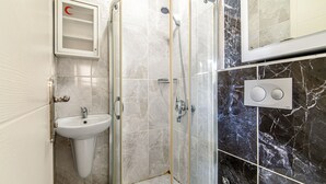 A bathroom with a glass-enclosed shower, a pedestal sink, and a mirror with a control panel. - Şişli Suites (Istanbul)