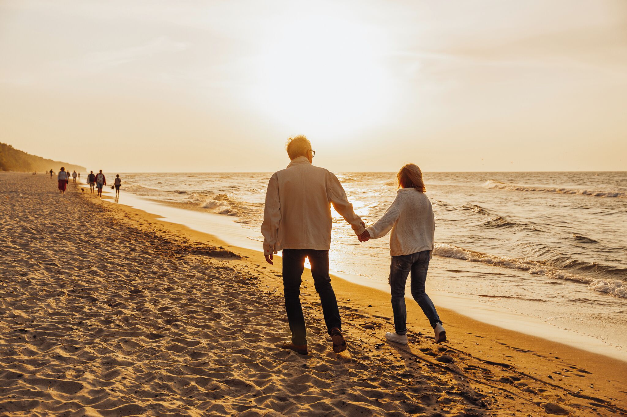A couple walking hand in hand on a sandy beach with the ocean in the background.