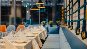 Un restaurant avec des tables dressées pour le service, un éclairage au plafond et un espace réservé aux clients, délimité par une barrière en corde.