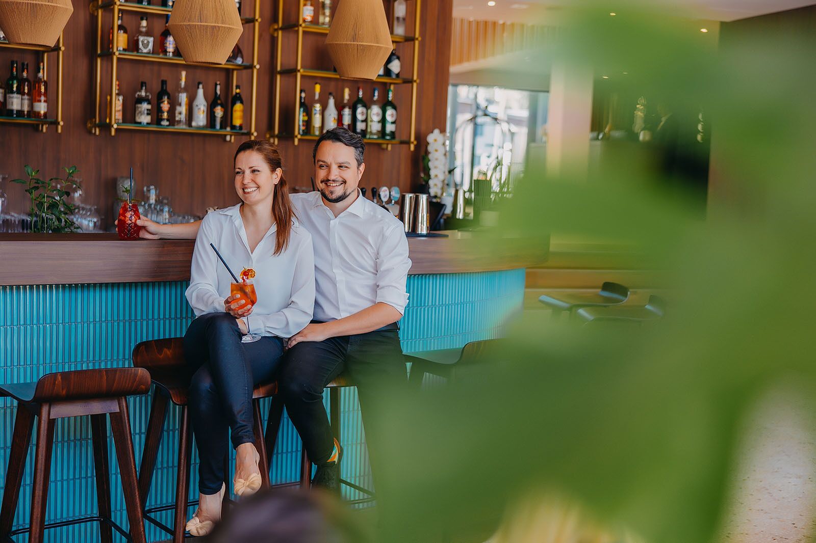 A couple seated at a bar with a wooden backdrop and shelves of bottles.