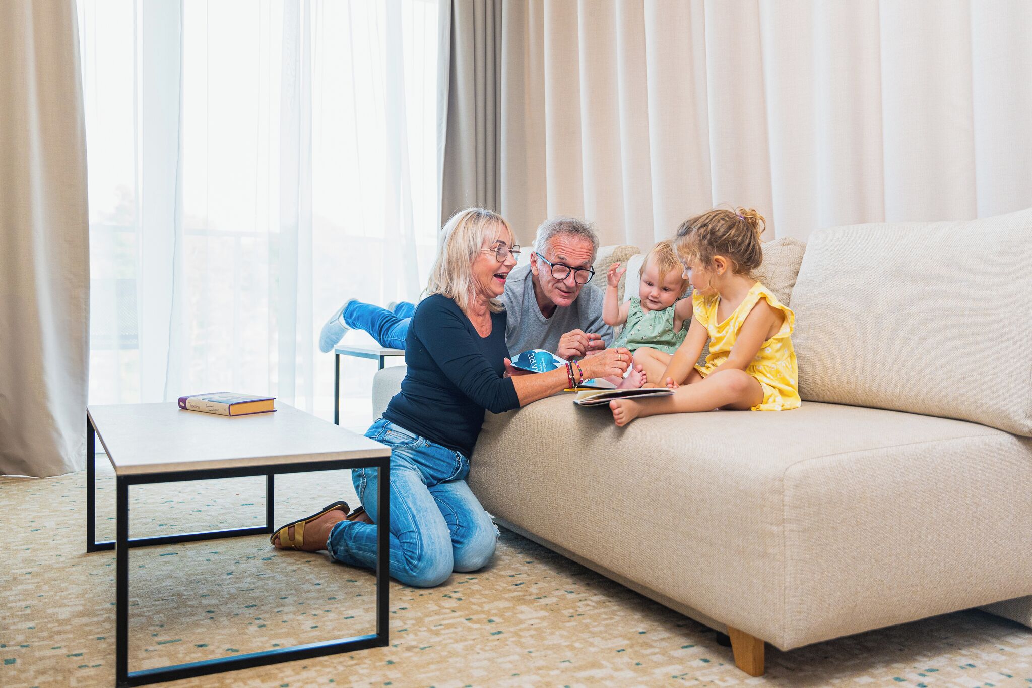A family of four on a beige sofa with a small table in front.