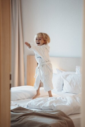 A child in a white robe standing on a bed in a hotel room.
