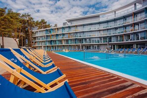 A modern hotel with a pool area, multiple balconies, and a wooden deck with sun loungers.