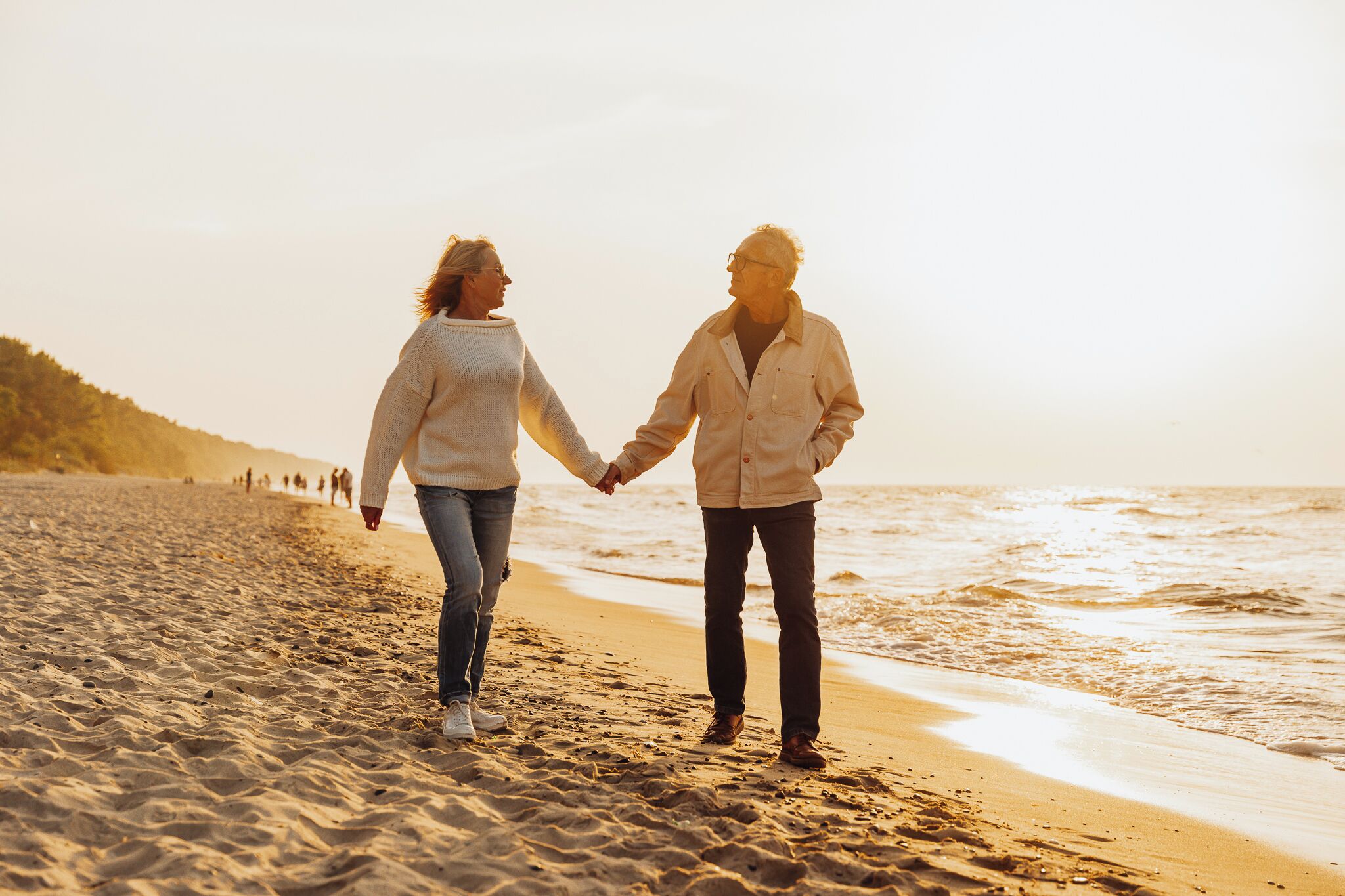 Two people holding hands on a sandy beach with the ocean in the background.