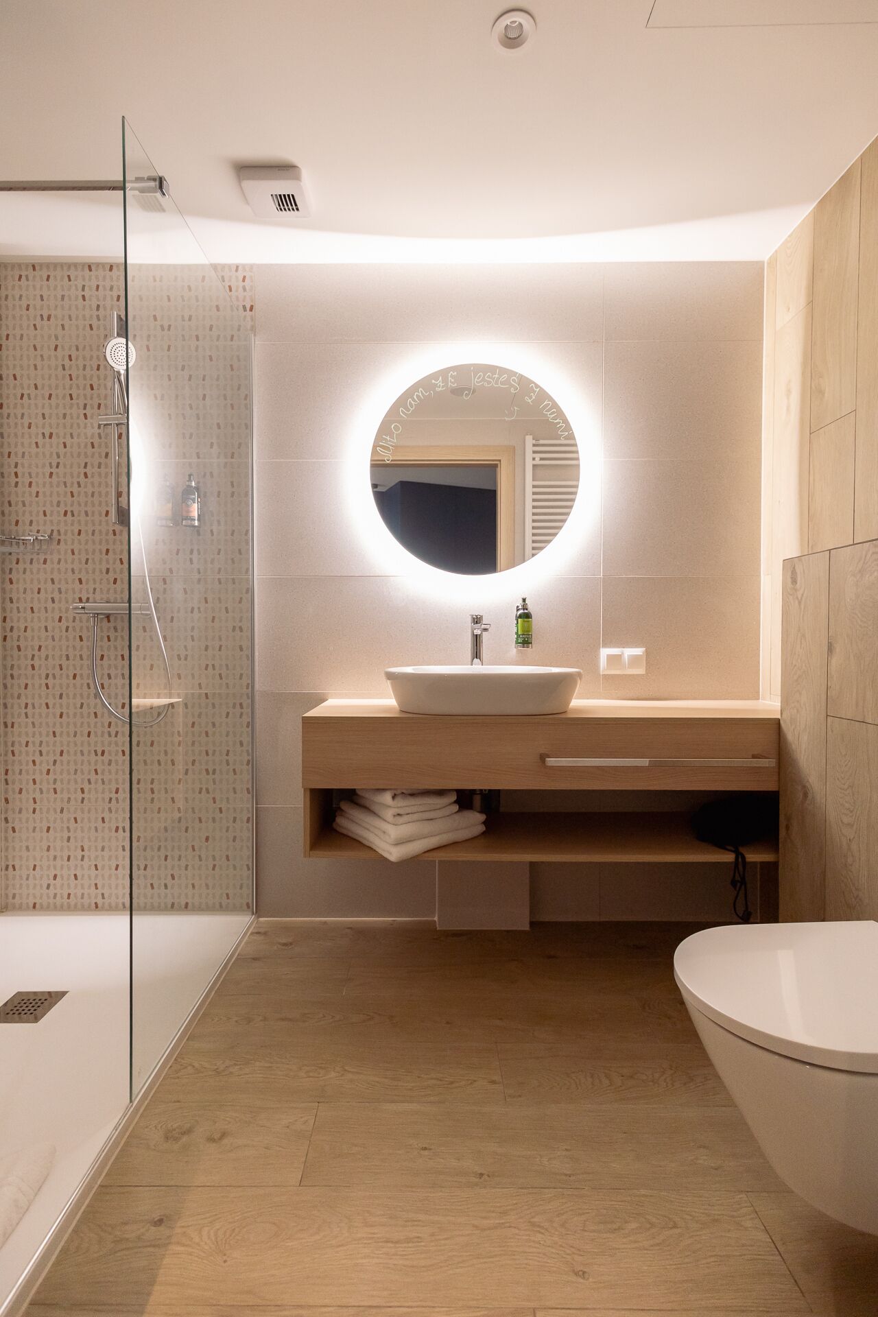A modern bathroom with a glass shower enclosure, a freestanding bathtub, and a vanity with a round mirror.
