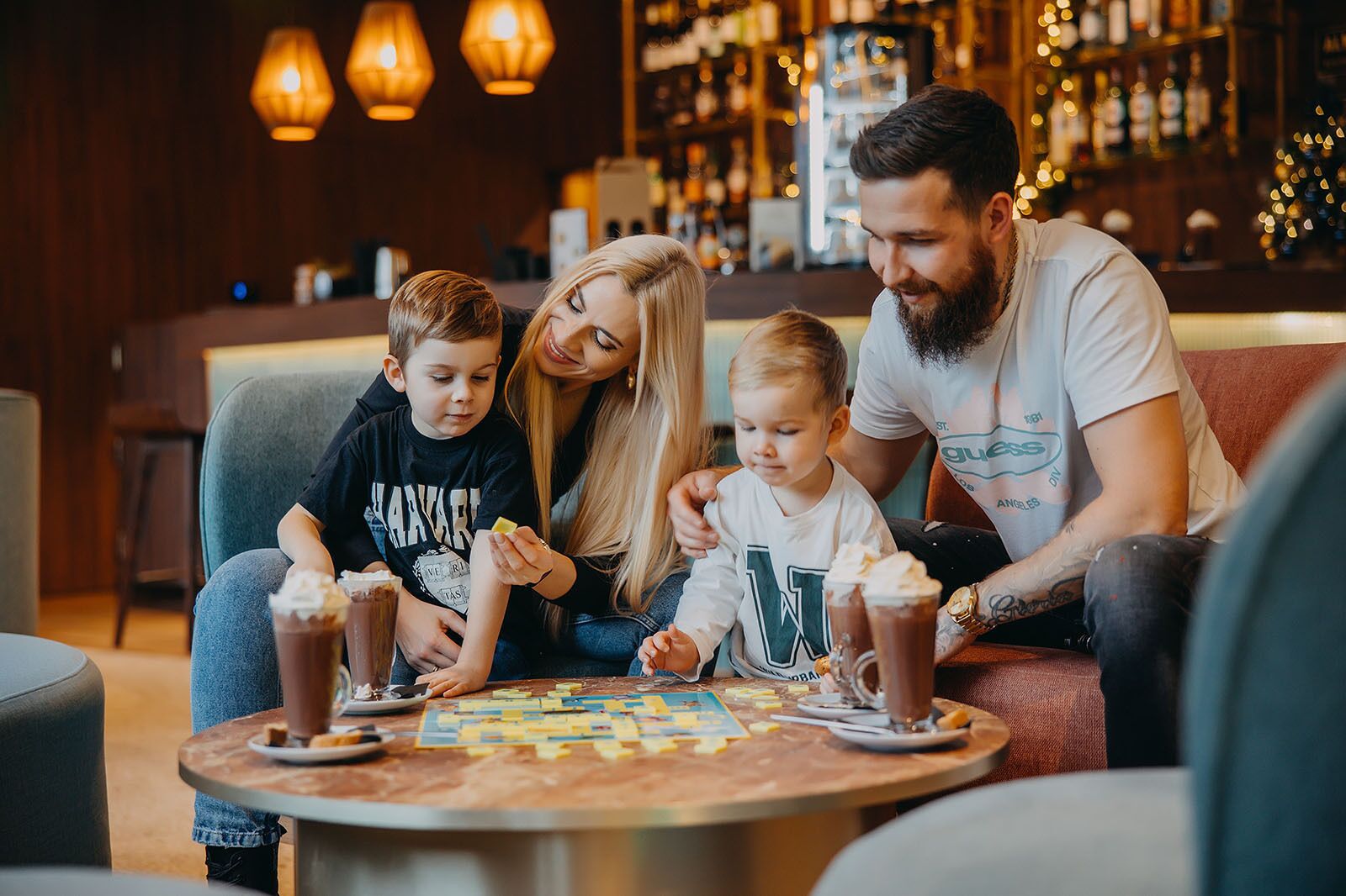 Una familia sentada a una mesa con bebidas y un juego de mesa en un ambiente interior acogedor.