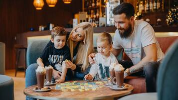 Una familia sentada a una mesa con bebidas y un juego de mesa en un ambiente interior acogedor.