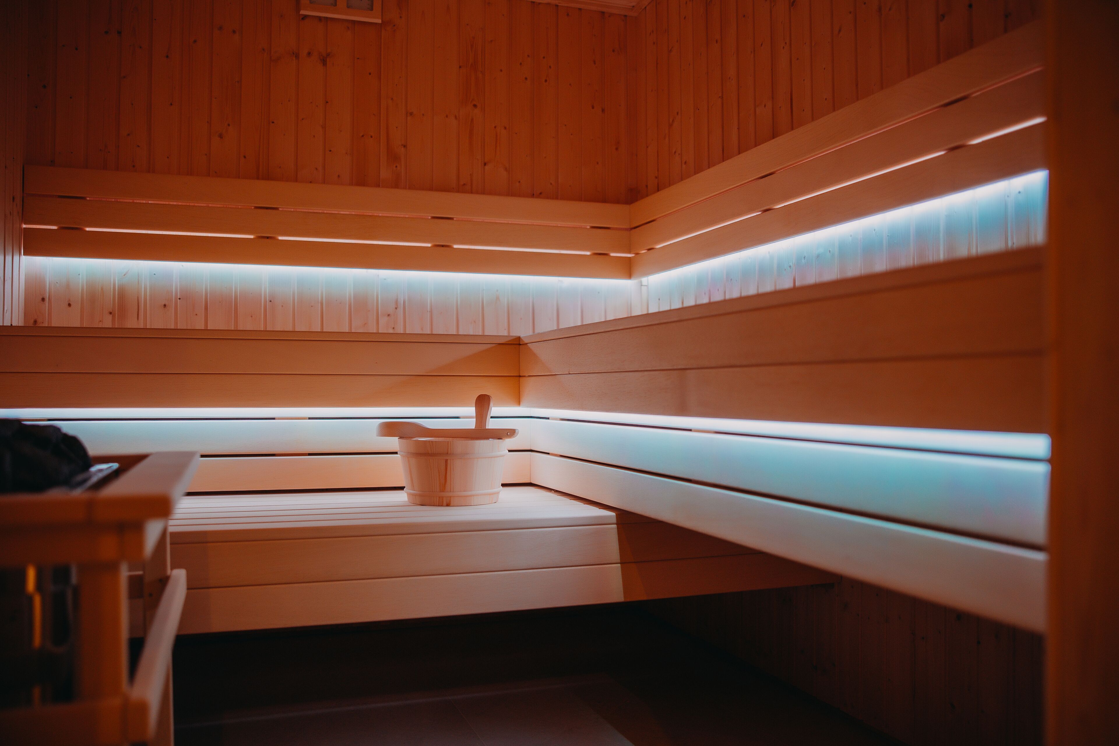 Una sauna con bancos de madera, una mesa de madera y un cubo con una cuchara.