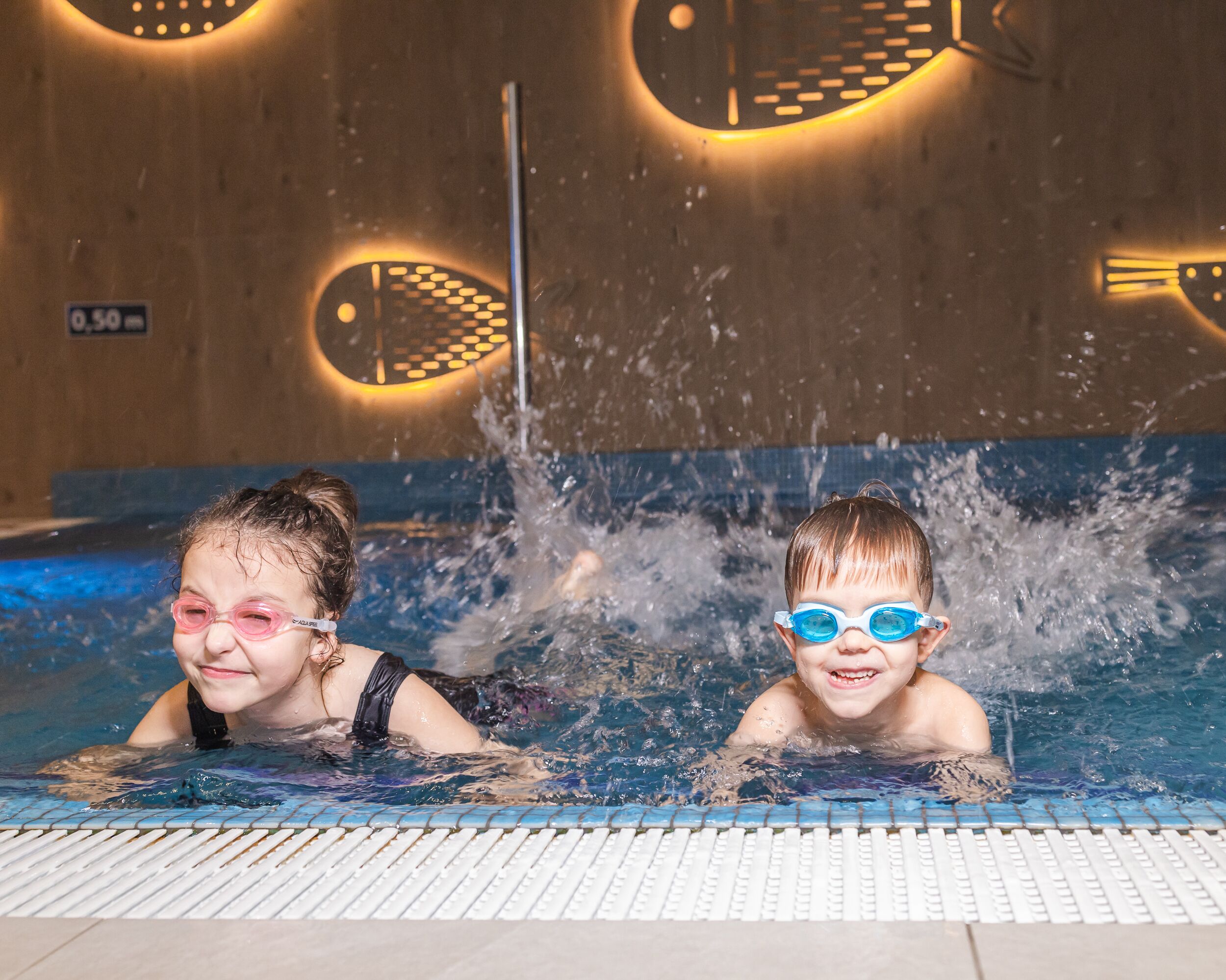 Two children in a swimming pool with water splashing around them.