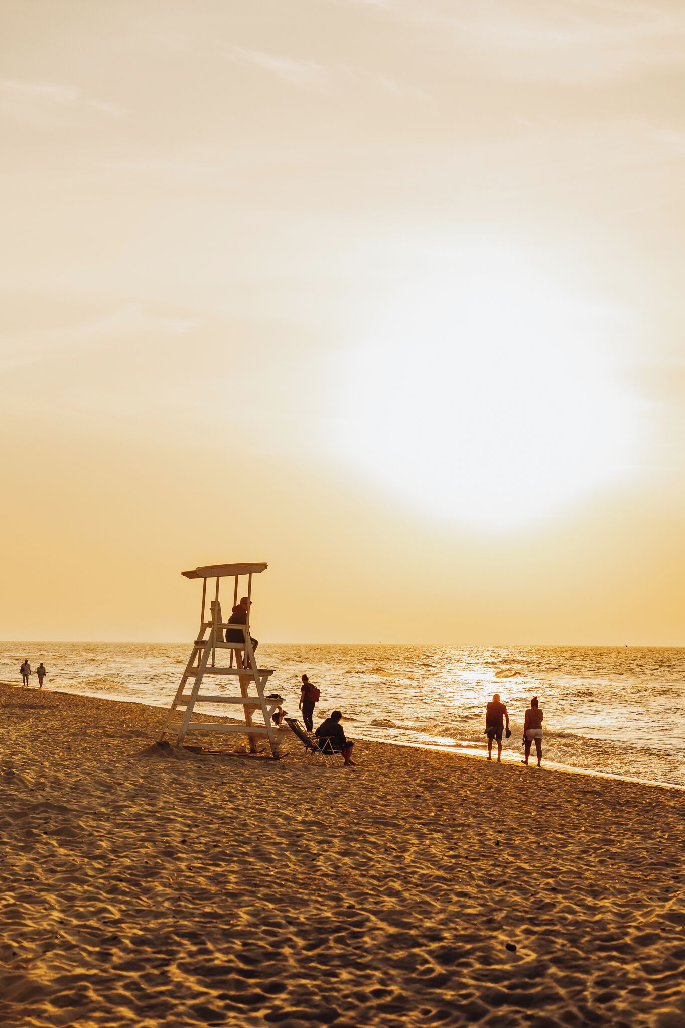 A lifeguard tower on a beach with people walking and sitting near the water.