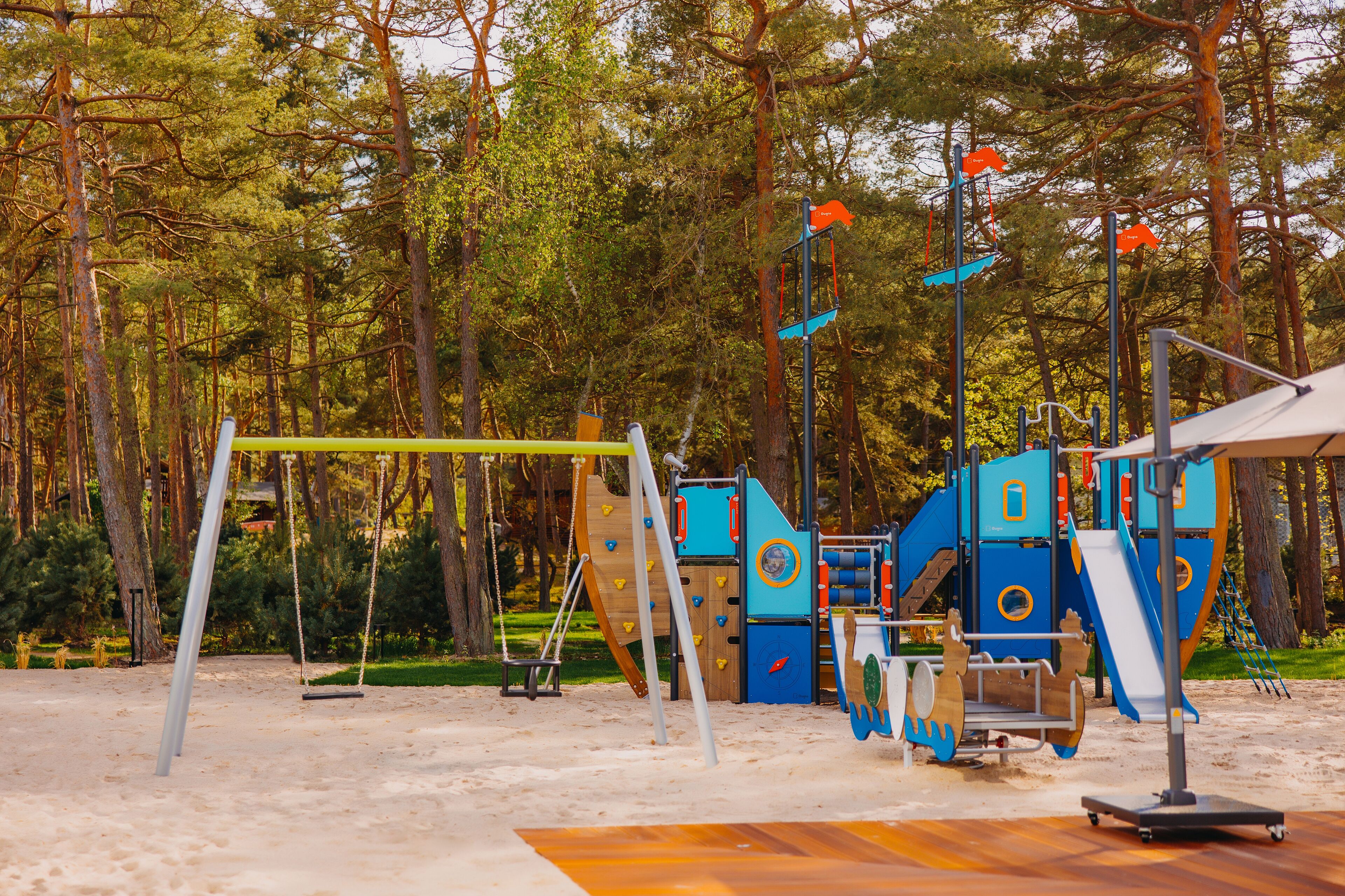 Un parque infantil con columpios, estructuras para escalar y toboganes, rodeado de árboles.