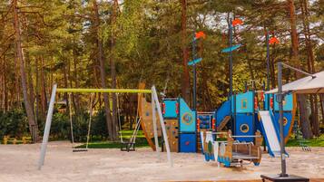 Un parque infantil con columpios, estructuras para escalar y toboganes, rodeado de árboles.