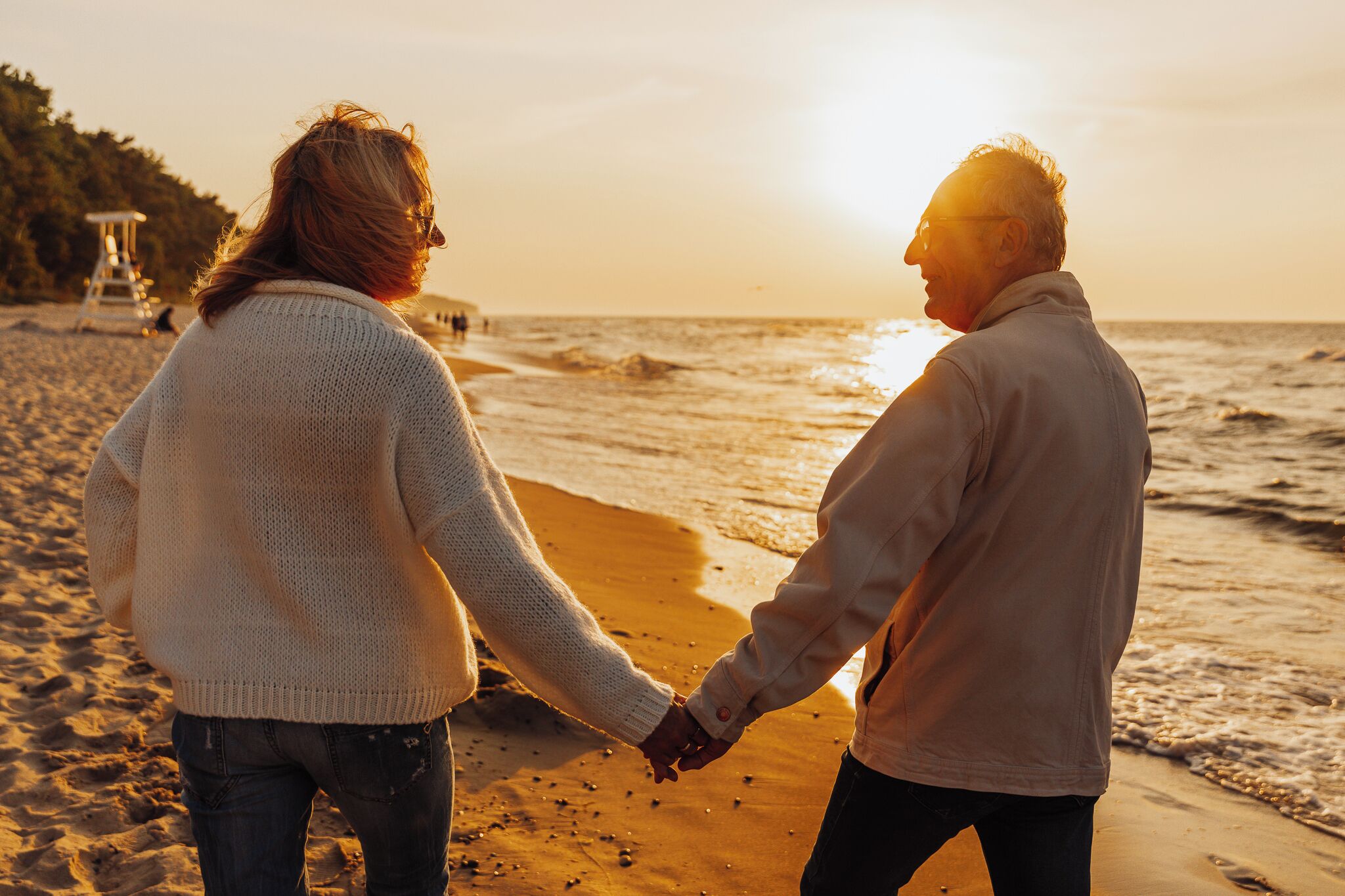 Un couple se tenant la main sur une plage, avec le soleil couchant en arrière-plan.