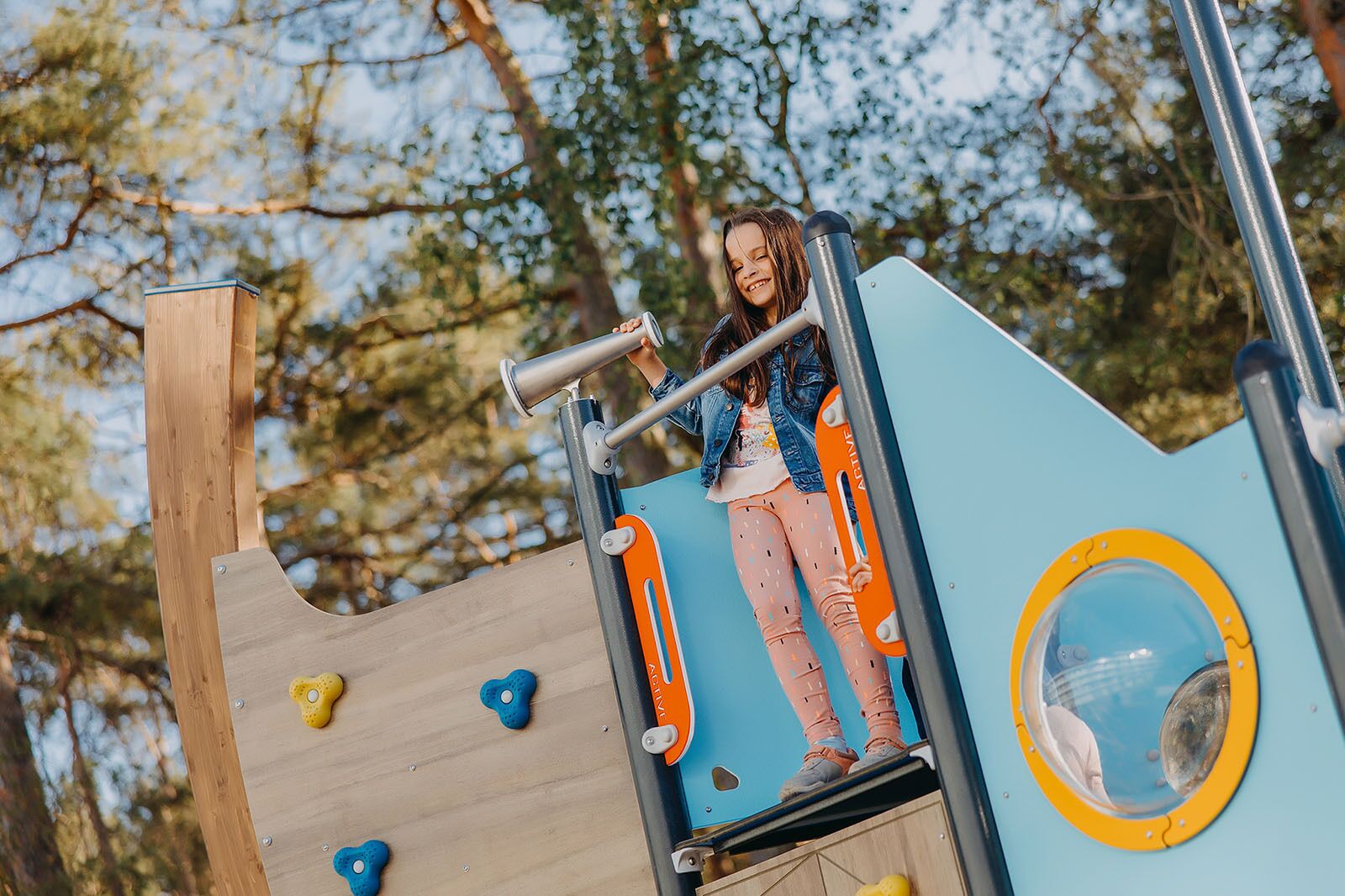 A child climbing a playground structure with a slide and climbing holds.