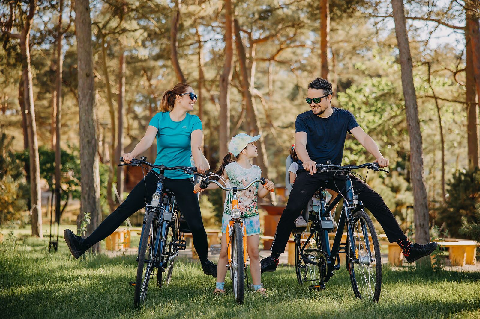 Tres personas en bicicleta en un parque con árboles y césped.