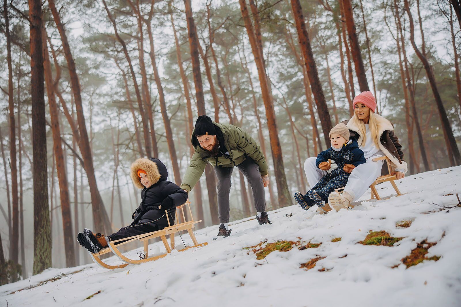 Escena nevada al aire libre con un trineo de madera, un bosque de fondo y gente disfrutando de actividades invernales.