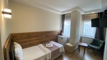 Habitación de hotel con cama de cabecera de madera, una mesita de noche pequeña, un sofá, un televisor y una ventana con cortinas.