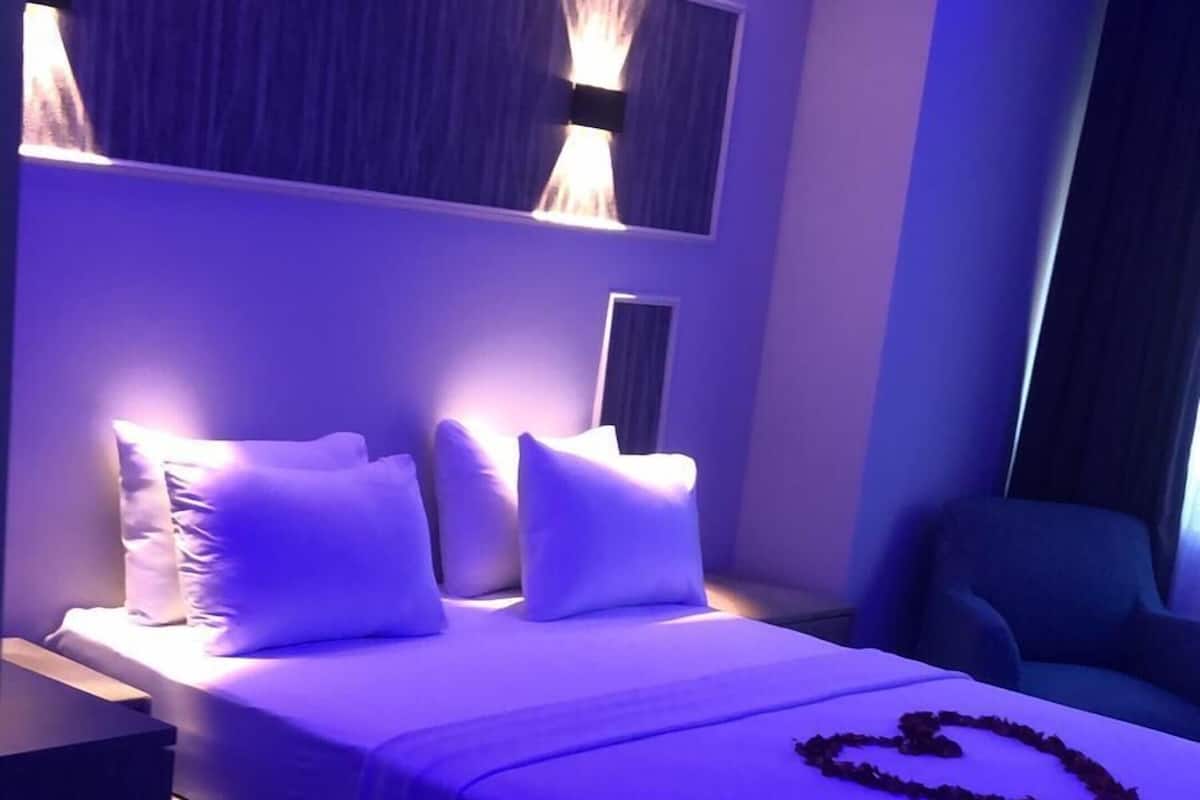 Un dormitorio con cama, almohadas, una mesita de noche y una decoración con forma de corazón sobre la cama.