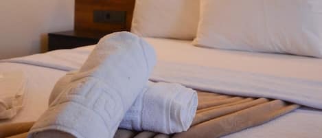 A neatly made bed with white linens and a folded towel on the bed.