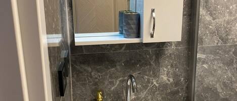 Un baño con un lavamanos blanco, un espejo encima y una pared de mármol.