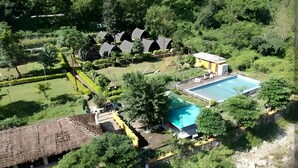 Vue aérienne d’un complexe hôtelier doté d’une piscine, de bâtiments à toits de chaume et d’une végétation luxuriante.