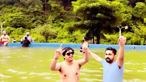 Deux personnes dans une piscine, avec en arrière-plan un paysage naturel et boisé.