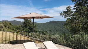 Eine Terrasse mit zwei Liegestühlen und einem großen Sonnenschirm mit Blick auf eine gebirgige Landschaft.