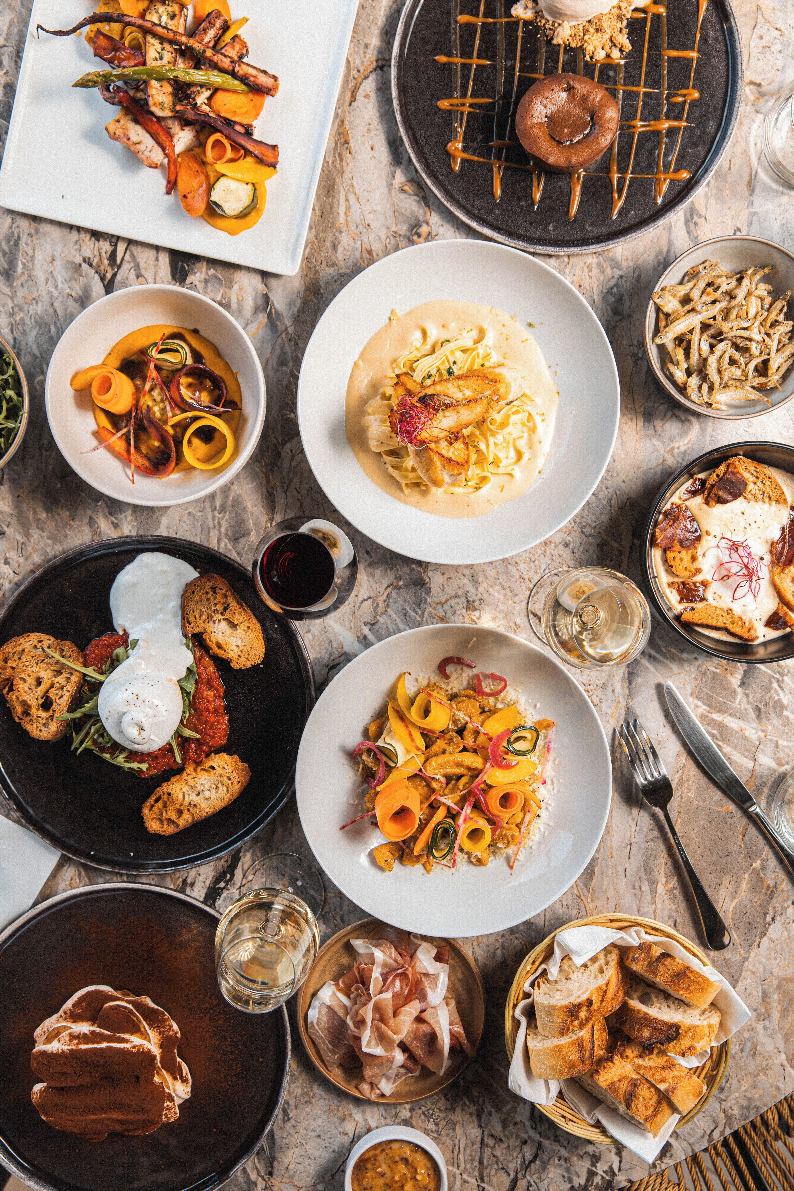 Variedad de platos sobre una mesa de mármol, como pasta, pan y un postre.