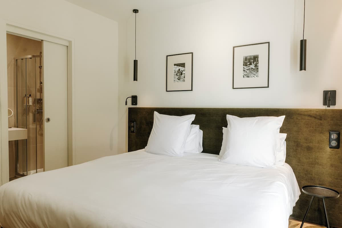 Un lit bien fait, avec du linge de lit blanc, une tête de lit en bois et deux tableaux encadrés accrochés au mur.