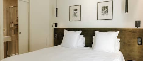 Una cama bien hecha con sábanas blancas, cabecera de madera y dos cuadros en la pared.