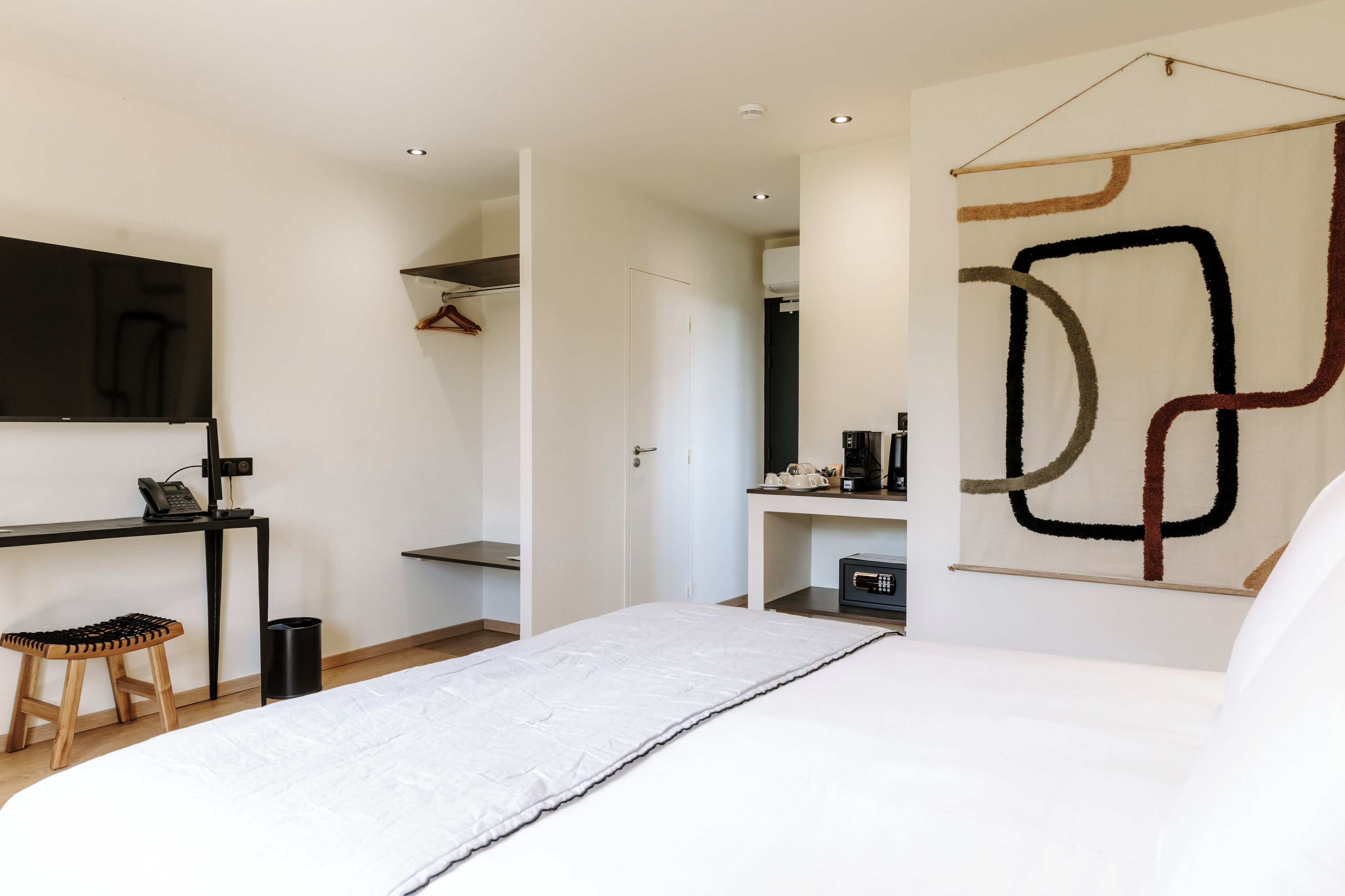 A modern bedroom with a bed, a desk, and a hanging abstract artwork.