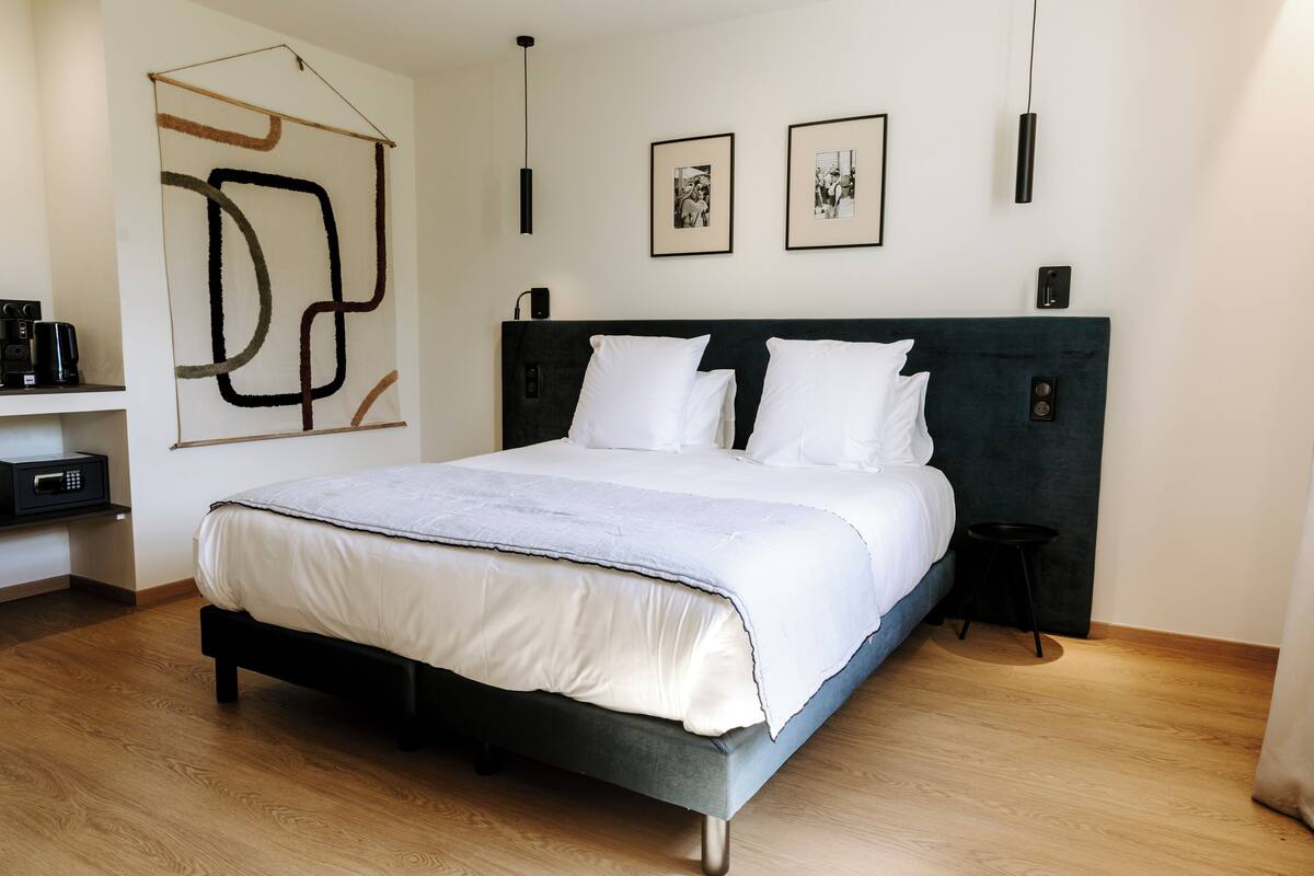 Une chambre d’hôtel moderne avec un grand lit, une tête de lit sombre et un design minimaliste.
