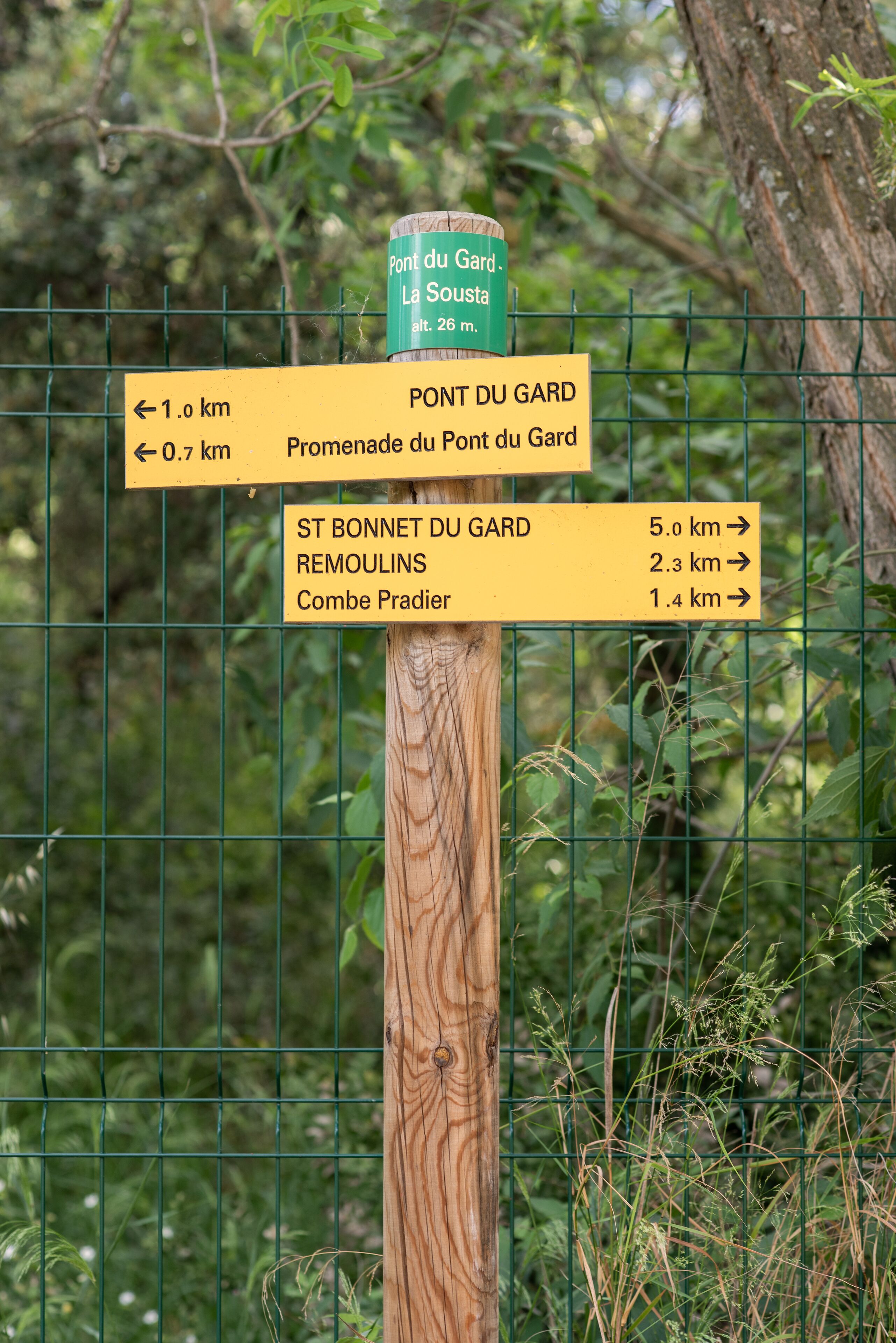 Un cartel de madera con indicaciones direccionales hacia Pont du Gard, Promenade du Pont du Gard, St Bonnet du Gard, Remoulins y Combe Pradien.