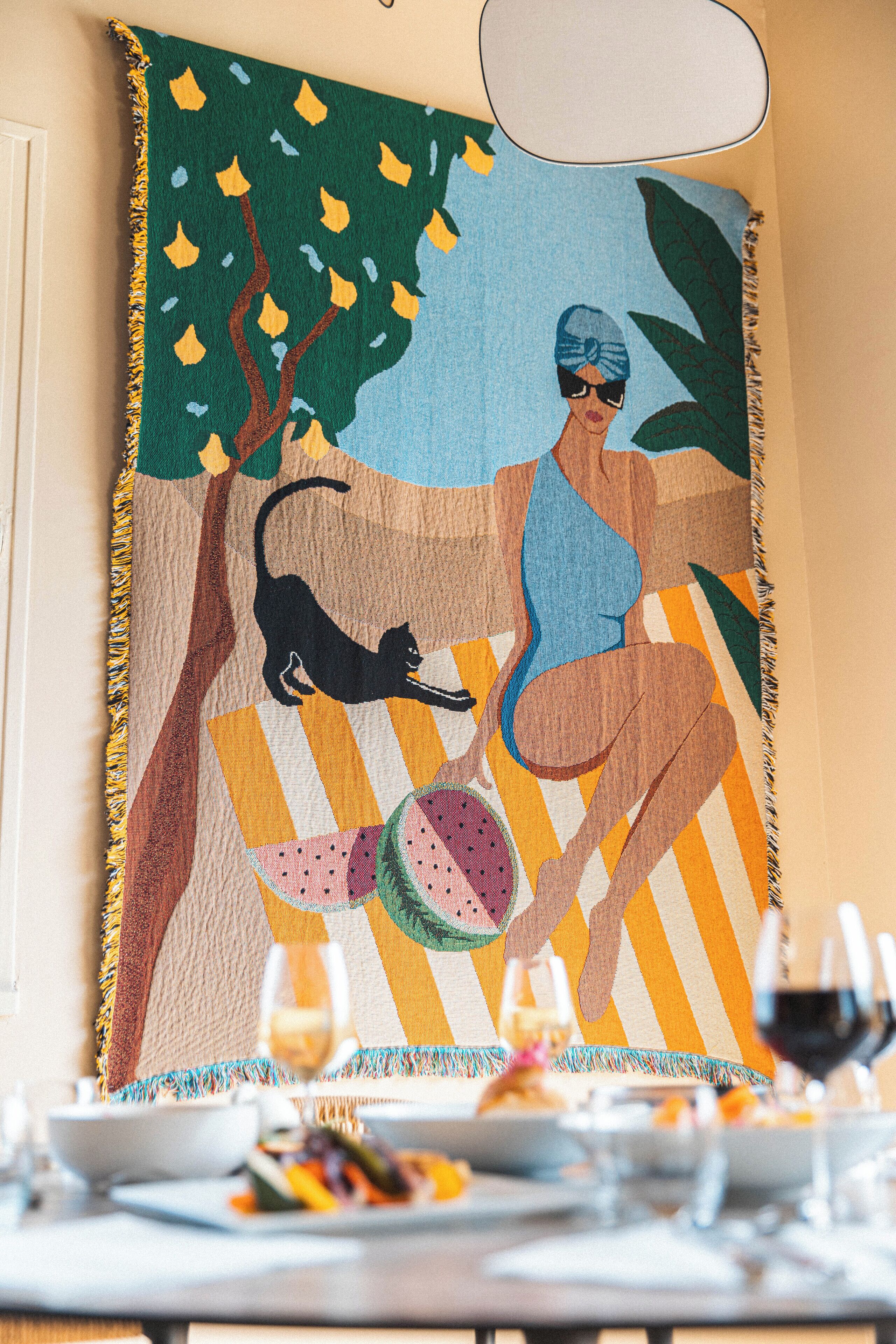 A dining table set with plates, glasses, and a colorful table runner with a tree and a cat.