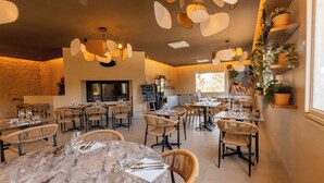 Un restaurante con mesas redondas, sillas de mimbre e iluminación colgante.