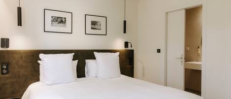 A neatly made bed with white linens and two pillows, a dark headboard, and two framed photographs on the wall.