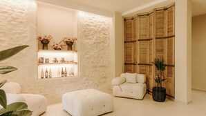 Una habitación moderna con pared de piedra, separador de madera y zona de estar con sofá y reposapiés blancos.