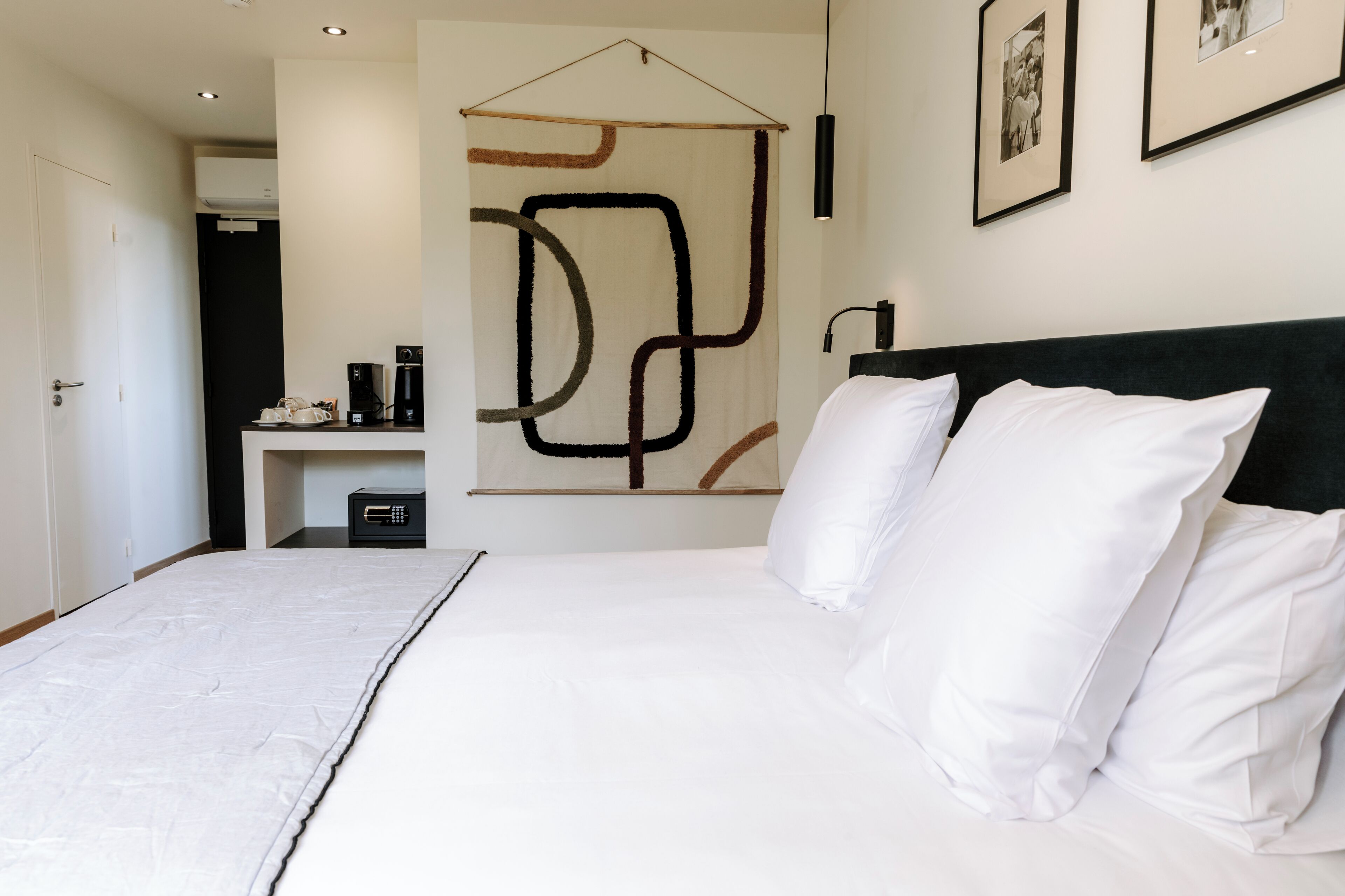 A modern hotel room with a large bed, white bedding, a black headboard, and abstract wall art.