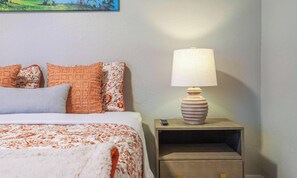 Un lit bien fait, avec une literie à motifs, une lampe de chevet et une petite table de nuit sur laquelle se trouve une télécommande.