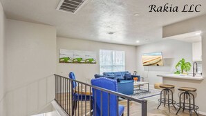 A modern living room with a blue sofa, a coffee table, and a TV. There is a staircase with a railing leading to another level. - 735 NW 30th St, Apt 11 OKC (Oklahoma City)