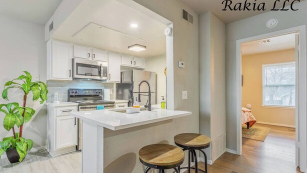 A modern kitchen with white cabinets, a central island with stools, and a view into a bedroom. - 735 NW 30th St, Apt 11 OKC (Oklahoma City)