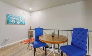 Un comedor con una mesa redonda de madera, dos sillas tapizadas en azul, una pequeña planta en maceta y una alfombra roja.