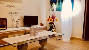 A dining area with a table, chairs, a flat-screen TV, decorative items, and a painting on the wall.