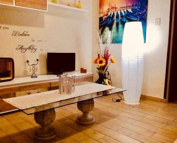 A dining area with a table, chairs, a flat-screen TV, decorative items, and a painting on the wall.