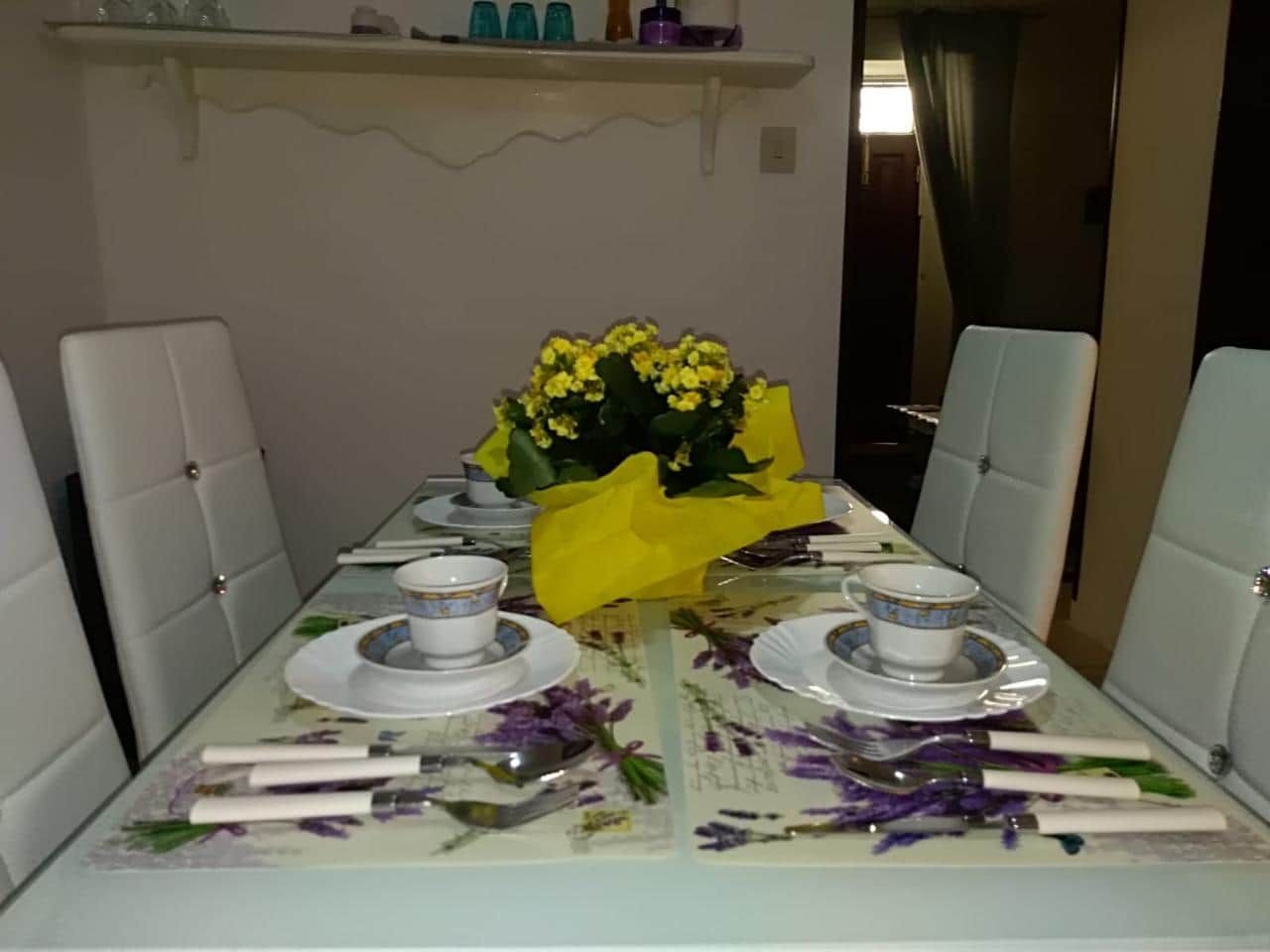 A dining table set for four with white chairs, a floral tablecloth, and a yellow centerpiece.