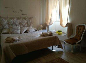 A bedroom with a bed, pillows, a nightstand, a chair, and a window with curtains.