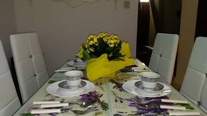 A dining table set for four with white upholstered chairs, a floral tablecloth, and a yellow floral centerpiece.