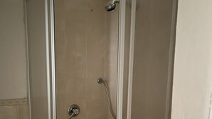 A glass-enclosed shower stall with a handheld showerhead and a fixed wall-mounted faucet.