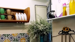 A kitchen with a sink, a stove, and a shelf with cups and a vase of flowers.