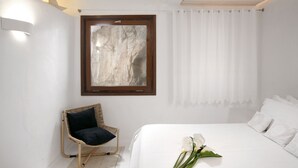 A bedroom with a bed, a wicker chair, a framed artwork, and a curtain.
